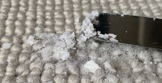 Close up of a neutral carpet with hardened wax being gentle scraped with a blunt knife to show how to get wax out of a carpet