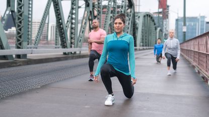 Group of four people dressed for running doing lunges on an urban bridge