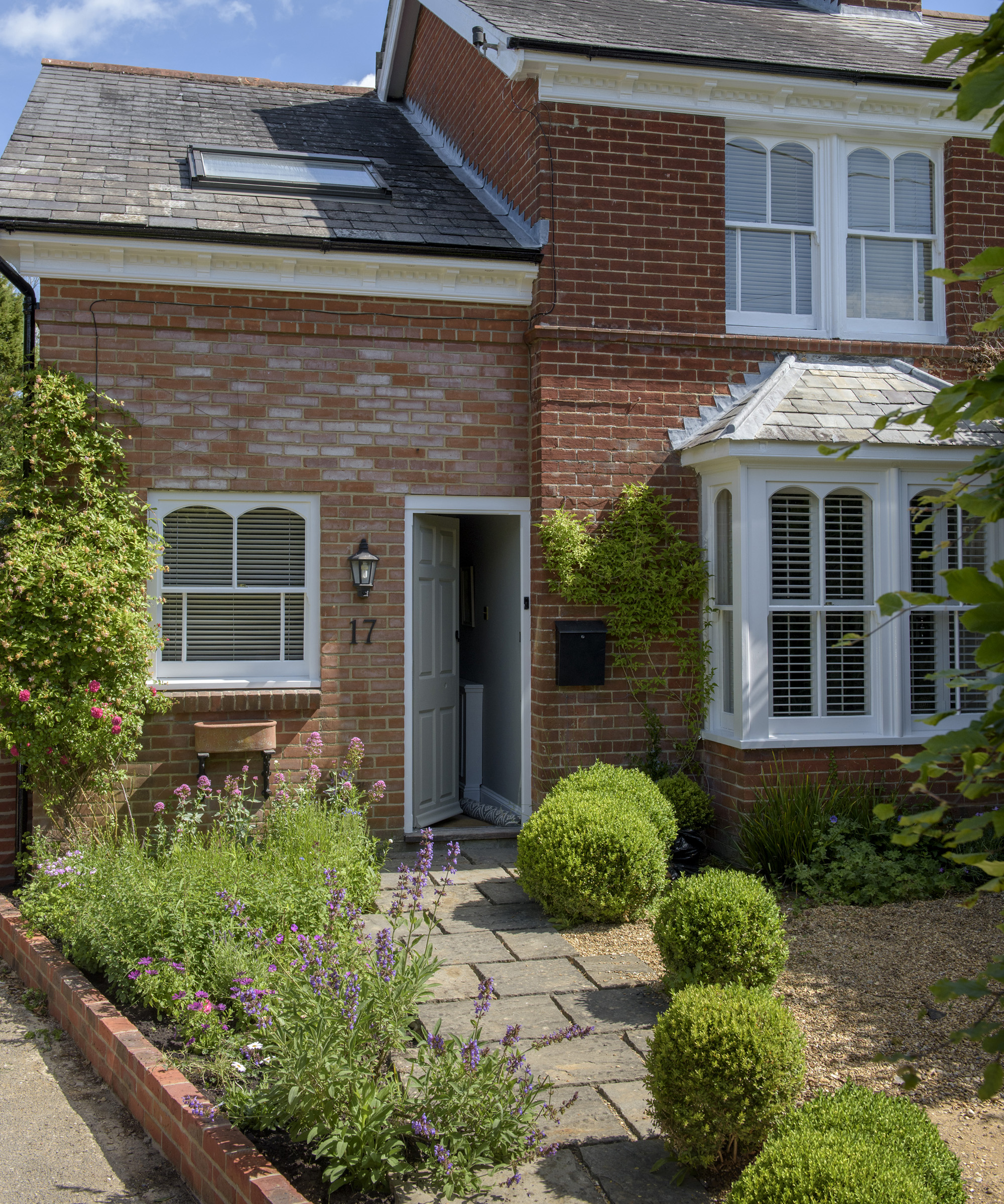 An example of very small front garden ideas with paving, gravel pebbles and low level topiary in front of a red brick house.