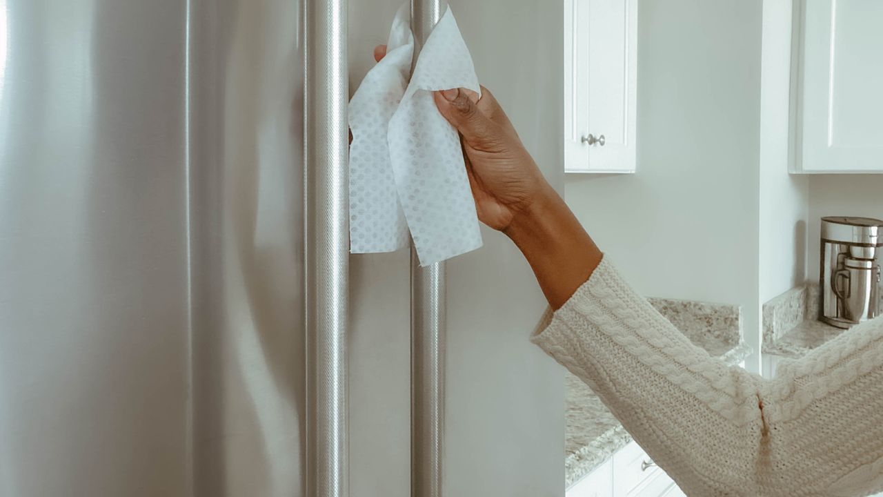 Cleaning a stainless steel fridge handle with an antibacterial wipe