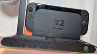 Photo of the Switch 2 dock sitting in a black charging stand, with yellow LED lights glowing around it.