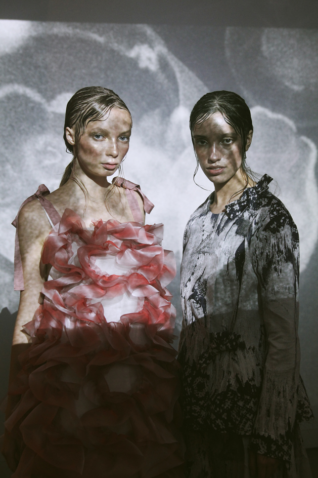 Models wear asymmetrical pleated dresses in red, white and black