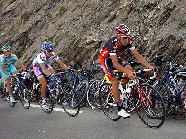Bikes of cyclo-tourists are parked while Pereiro, Valjavec and Kashechkin (r-l) ride by.