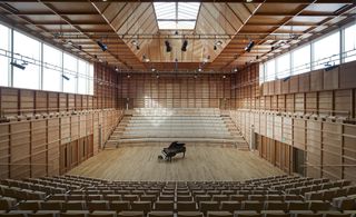 An amphitheater with a piano in the middle of a wooden floor with seating stands on either side.