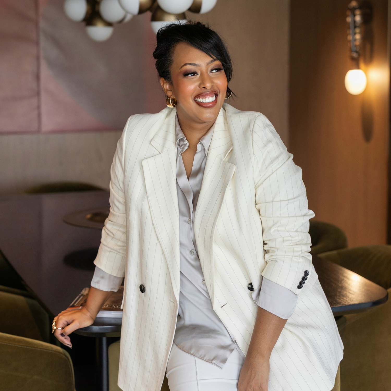 A woman in a white pinstripe suit, leaning against a table