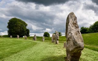 Visitor touching a Neolithic standing monolith at Avebury Henge England south west sector edge of the largest megalithic stone circle in the world Avebury, Wiltshire, England - June 9, 2019