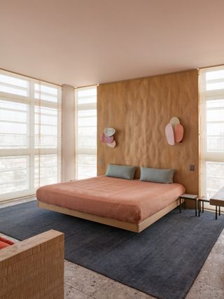 bedroom with floating wooden bed with brown feature wall behnd it, with linen curtains covering the full legnth windows either side of the bed and on the wall next to it
