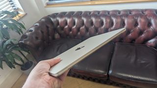 En hand håller upp den nya MacBook Air 13" på ett café med locket stängt.