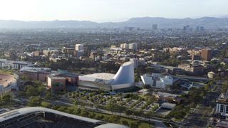 artist's illustration of a large complex of white buildings in a sunny city, with mountains in the background