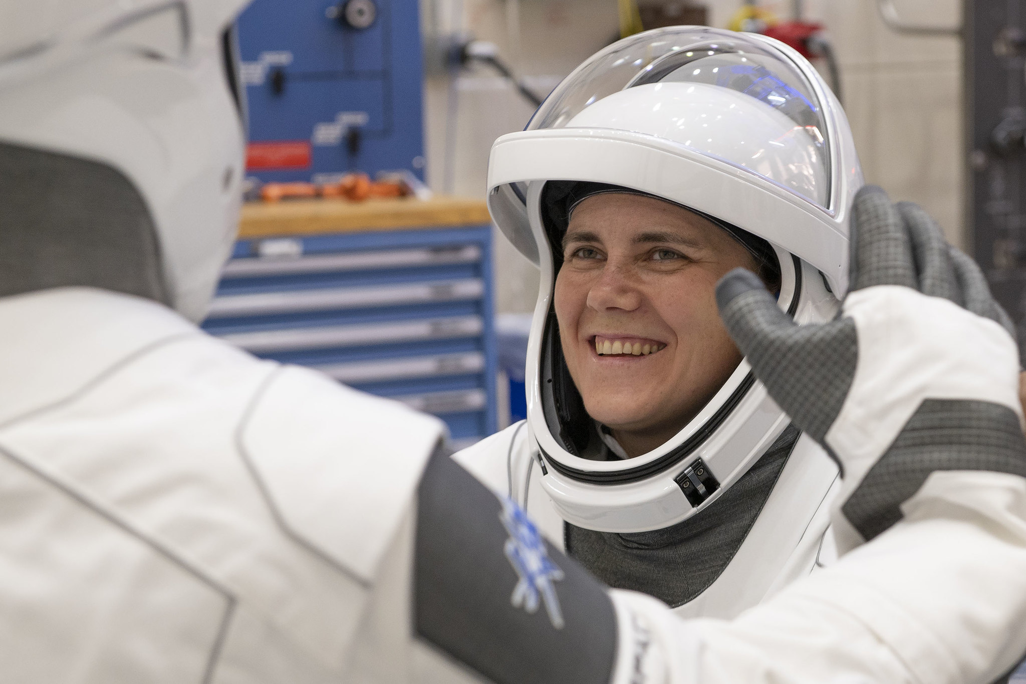 astronaut in white suit smiling, with another astronaut in white suit in front with the back showing