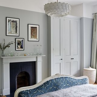 an elegant looking bedroom with light grey walls, triple white slim doors, black fireplace with white mantle, and a blue velvet decorative footboard on bed