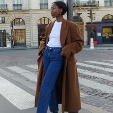 European influencer Sylvie Mus poses in Paris wearing a camel coat, white T-shirt, and dark-wash jeans