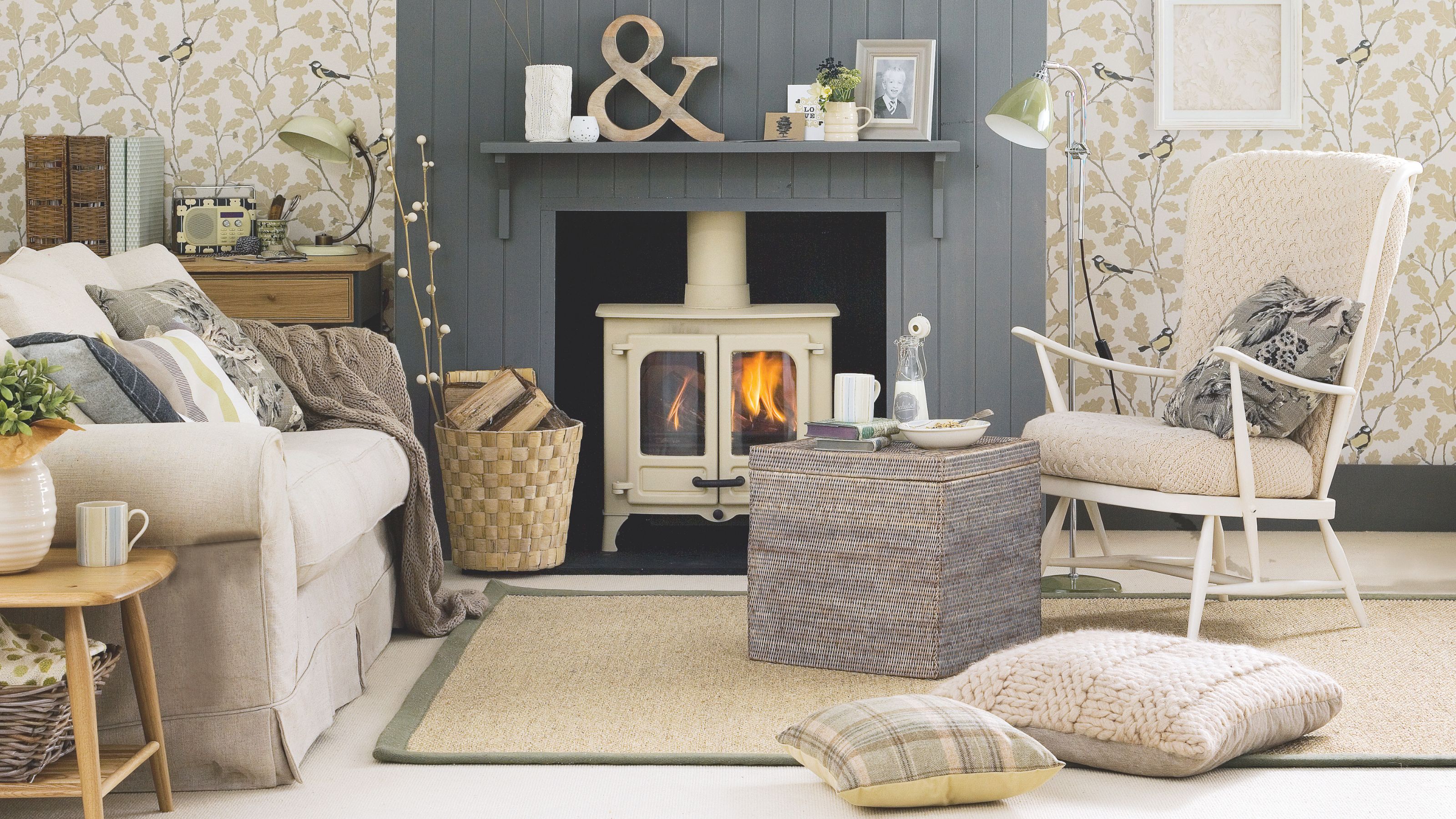 Cream log burner in with a blue-grey panelled surround in a light coloured living room, with patterned wallpaper