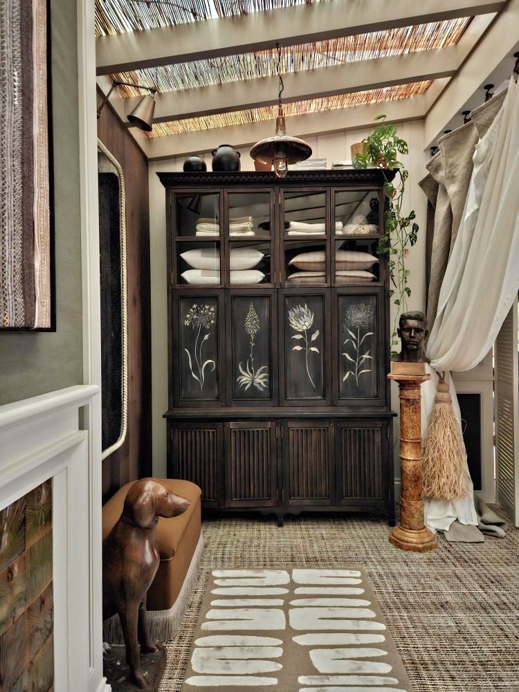 Image of a large wooden cabinet with white painted flowers on it. The room is a boho-inspired design with a skylight and a rattan rug.