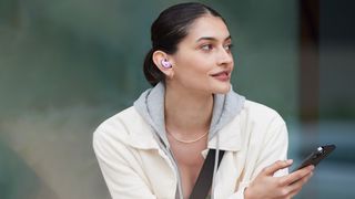 A woman wearing the beats fit pro earbuds in purple and holding a phone