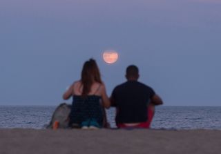 The Full Strawberry Moon and penumbral lunar eclipse of June 5, 2020 rises over the horizon as people enjoy the good weather at La Malagueta beach in Málaga, Spain.