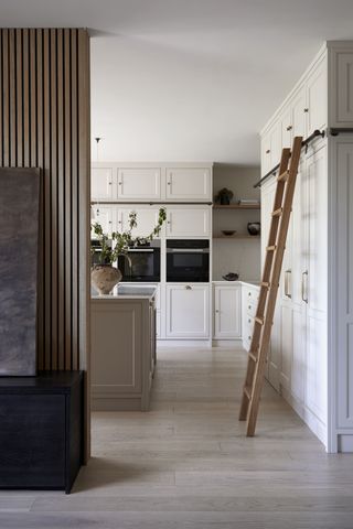 An open plan kitchen with white shaker cabinetry, a wooden slatted partition wall and a rail ladder