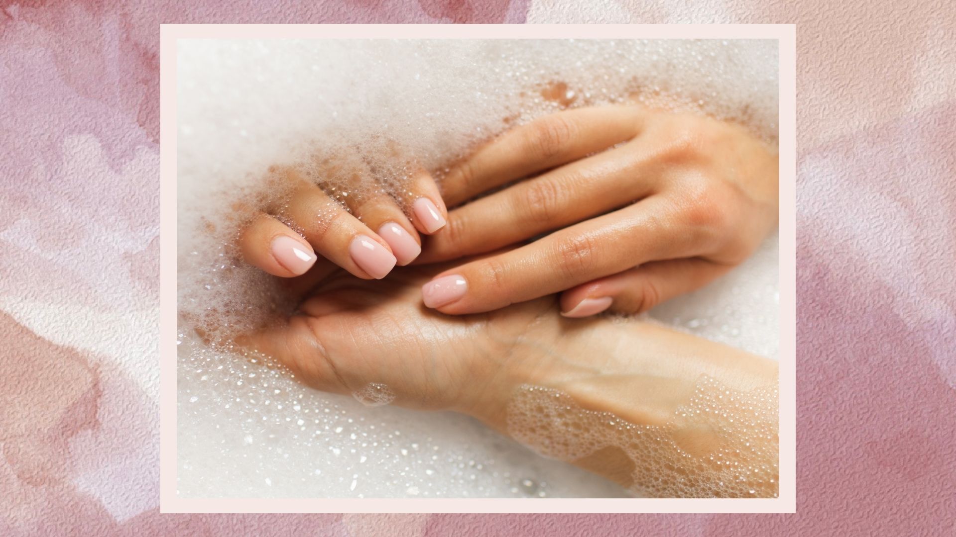 a pink watercolour frame containing an image of a woman&#039;s hands with a sheer pink manicure in bubbly water, washing them