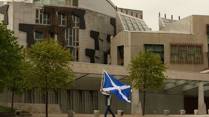 Man waving a flag in front of the Scottish Parliament. © Jeff J Mitchell/Getty Images