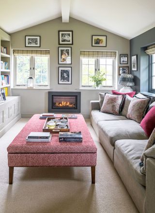 living room with grey sofa, pink footstool and fitted bookshelves and fire lit