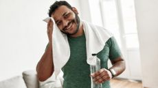 Man toweling his sweaty forehead and drinking water as part of his post-workout recovery