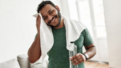 Man toweling his sweaty forehead and drinking water as part of his post-workout recovery