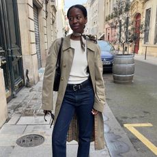 Influencer Sylvie Mus wears dark wash jeans, white tee, trench coat, and scarf. 