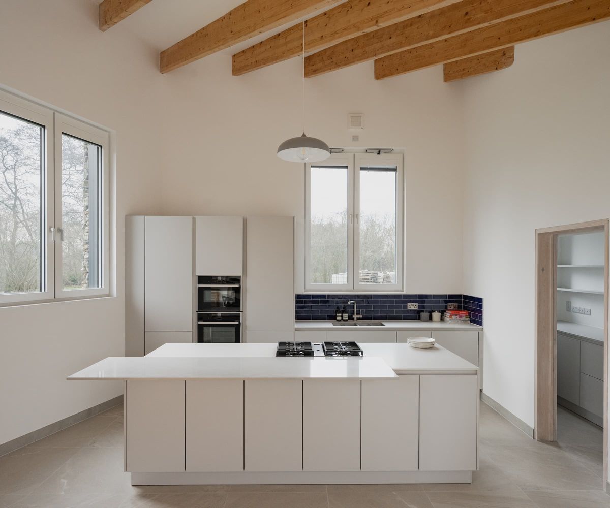 A white kitchen with wooden beams above and a white kitchen island with hob