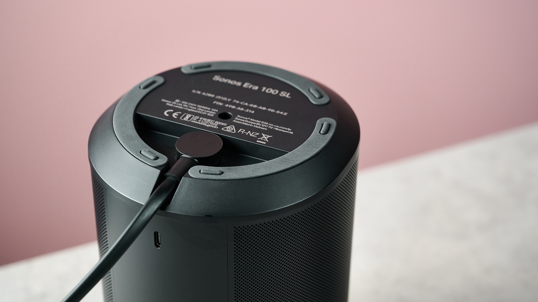 The bottom of the Sonos Era 100 SL, showing the power port and plugged in cable.