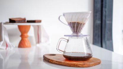 One of the key coffee makers in the pour-over vs drip coffee debate, a pour over coffee maker with a filter cone on a white table with a wooden table in the background
