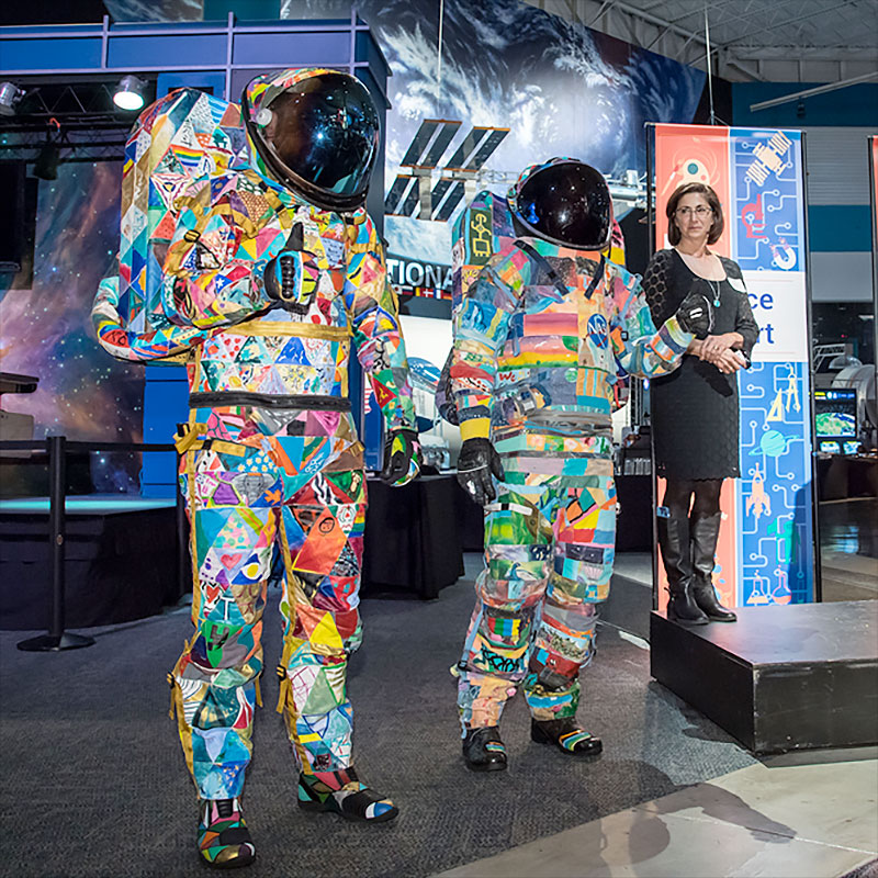 two people model in multicolor, patchwork spacesuits that were decorated by pediatric cancer students