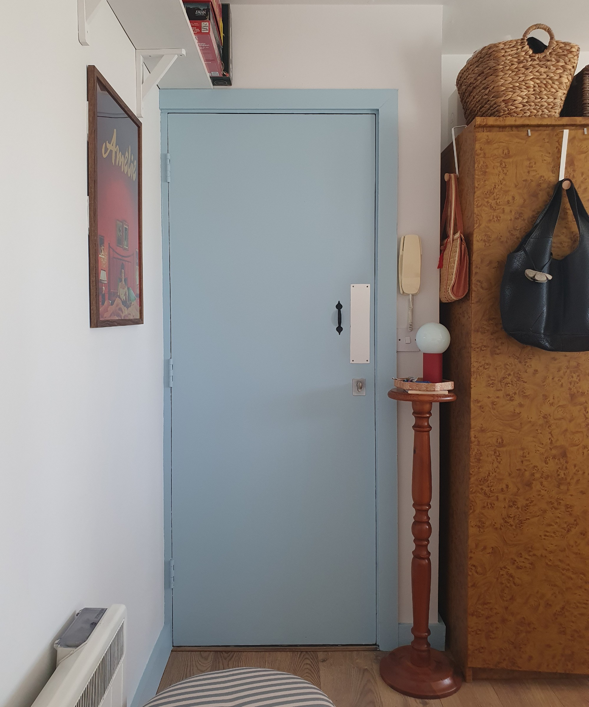 Sara's entrance area with a striped storage ottoman, a side table with a lamp next to the front door and a framed film poster hanging on the wall
