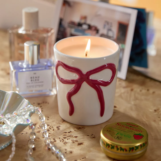 Bow candle holder in bedroom setting with perfurmes in background