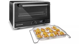 The KitchenAid countertop oven on a white background with the stainless steel air basket in front with fried food on