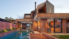 The outside of a home with a large pool and decking as well as stone paving in certain areas. You can also see the inside of the home. 