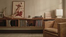 A living room with a textured accent armchair, a floating display of vinyl, a record player, a white table lamp, a leaning painting, and ceramics