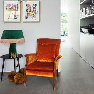 Burnt orange armchair next to green fringe lamp on small dark side table