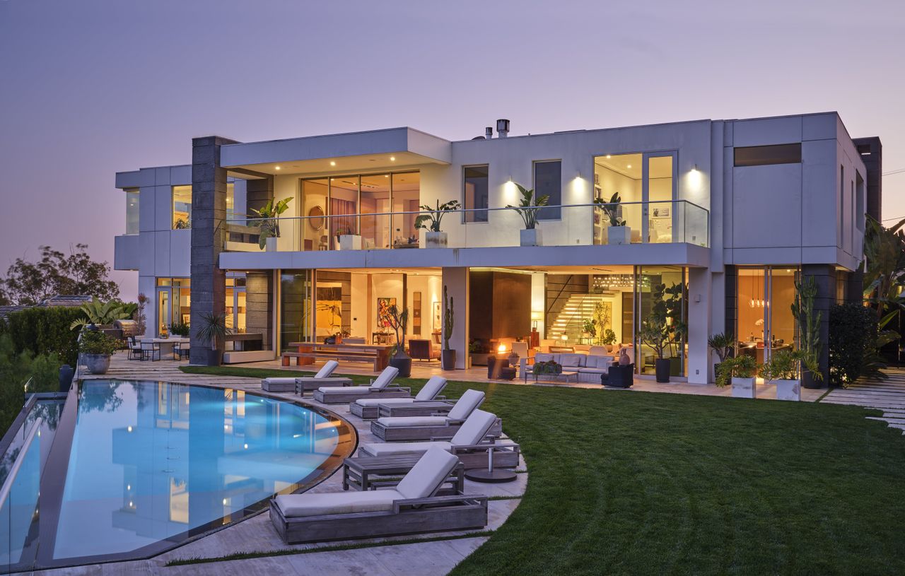 A exterior shot of a large house at dusk with a large garden and a pool