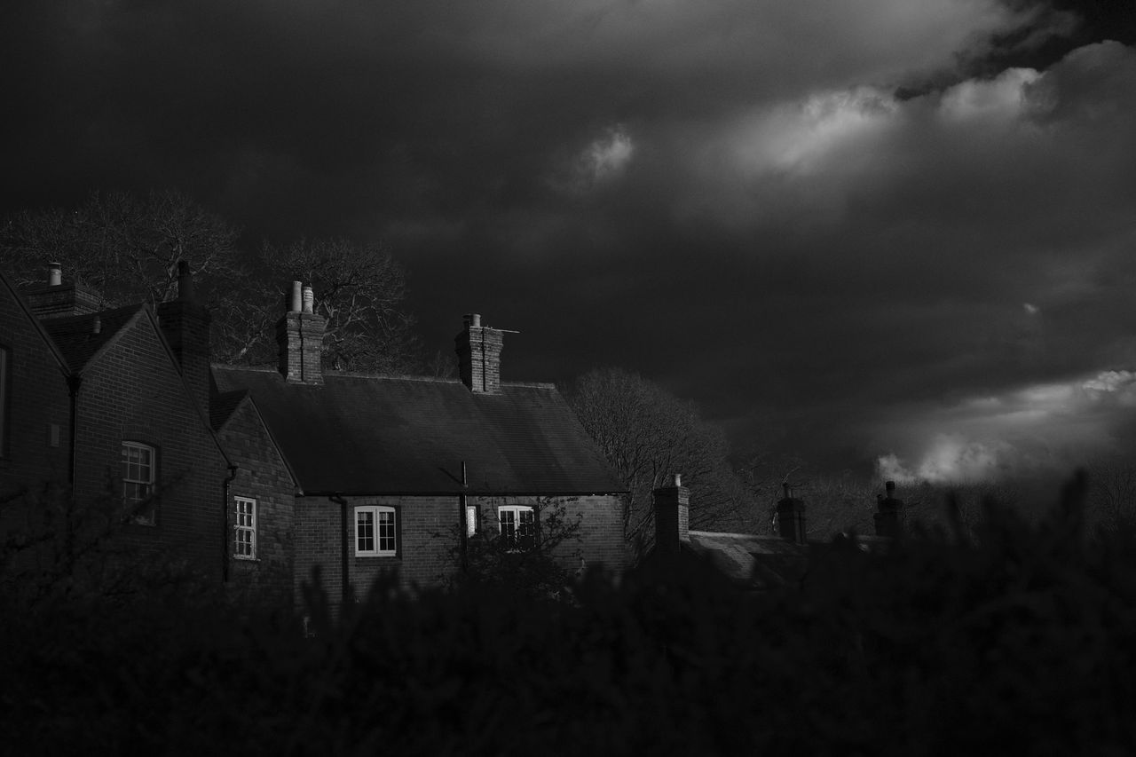 Top part of house llluminated by the sun with moody skies in black and white