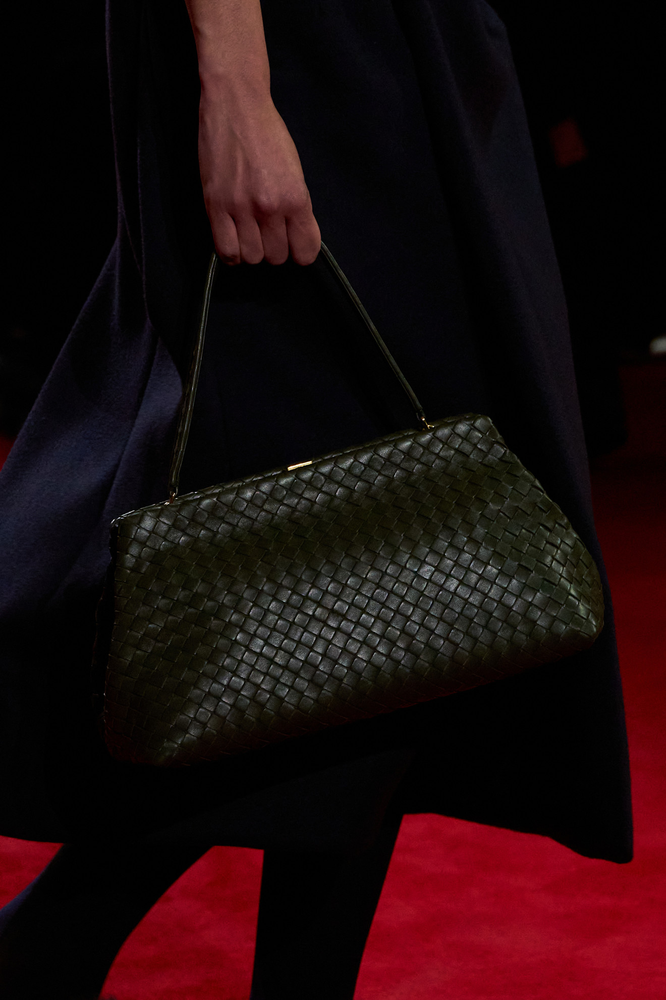 A close-up photo of a model walking in the F/W 26 Bottega Veneta show carrying a green intrecciato kisslock bag.