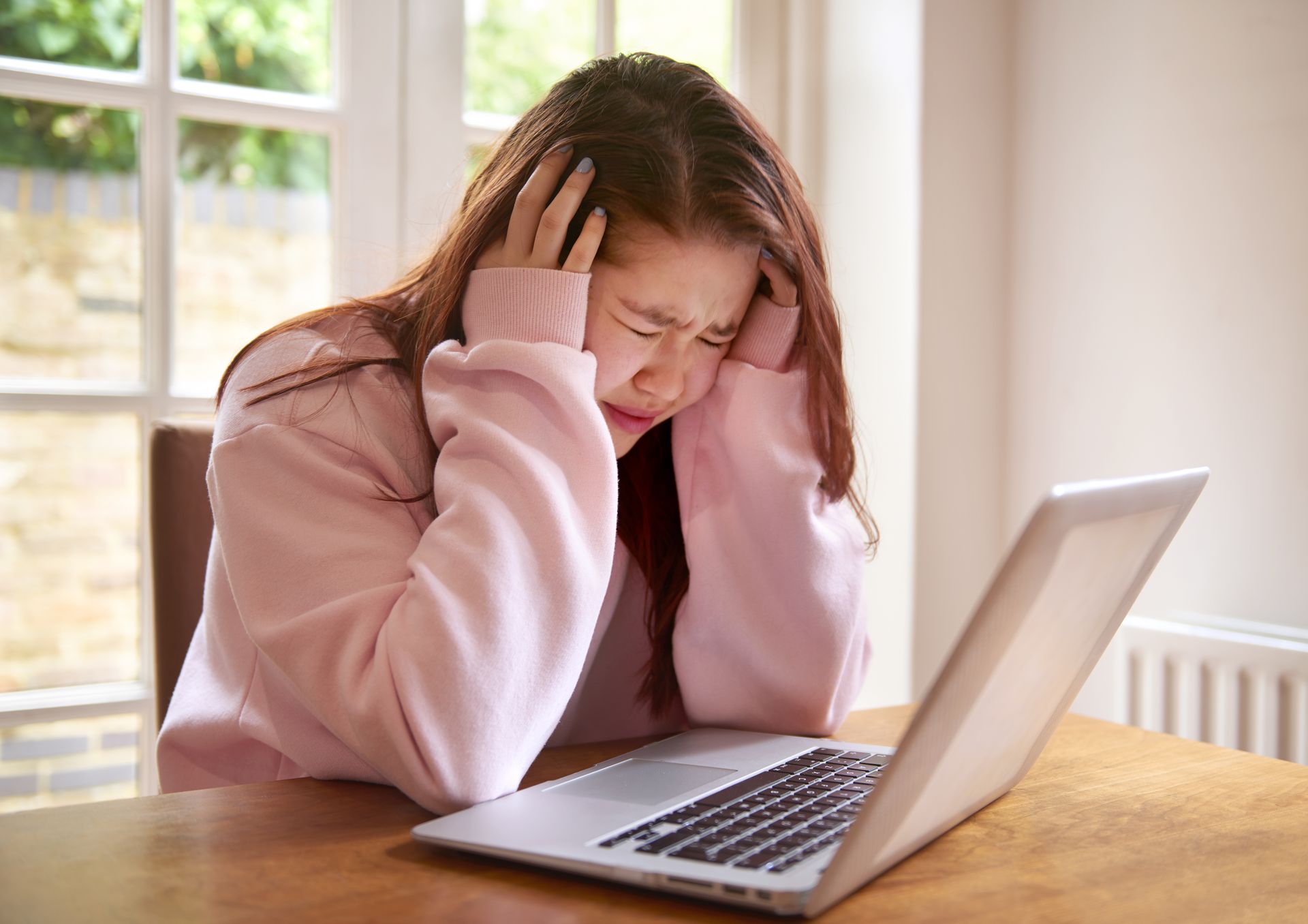 Teenager crying using laptop with a migraine