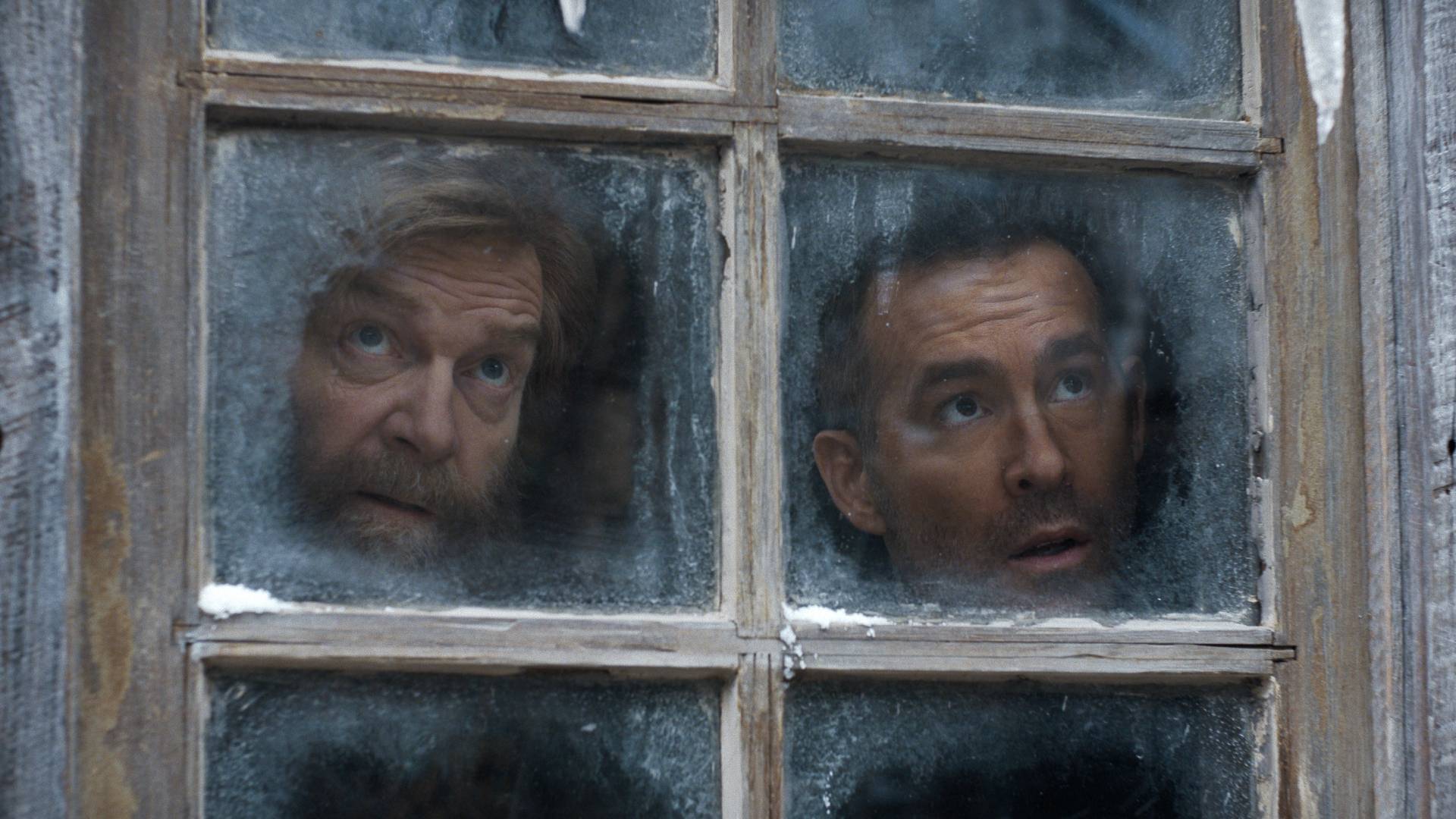 L to R: Kenneth Branagh as Nikolai Ustinov and Ryan Reynolds as Troy Kelly looking out of a frosted windown in Mayday