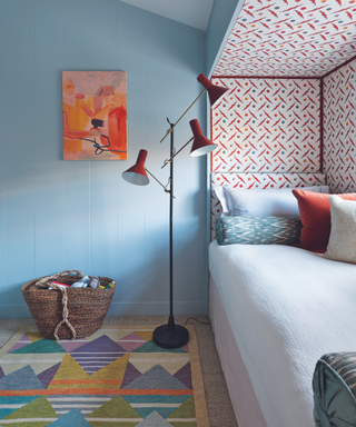 boxed in bed surrounded by patterned wallpaper in room with blue walls and patterned rug and red floor light
