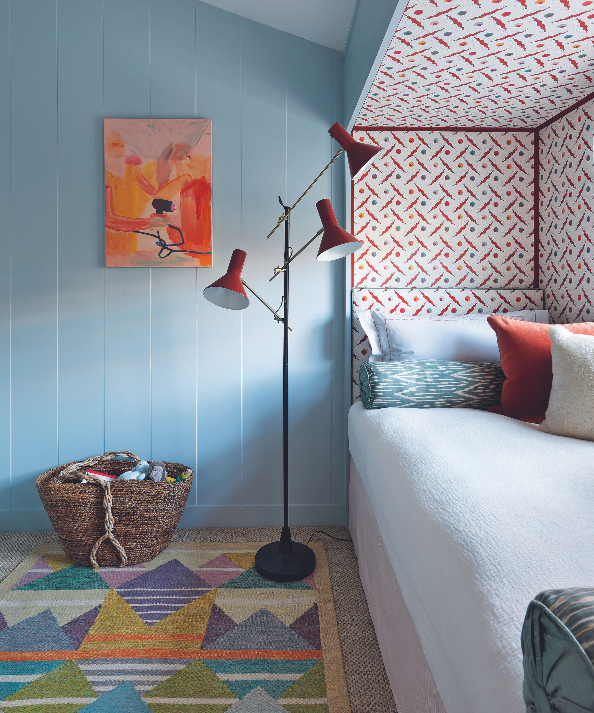 enfermé dans un lit entouré de papier peint à motifs dans une chambre avec des murs bleus, un tapis à motifs et un lampadaire rouge