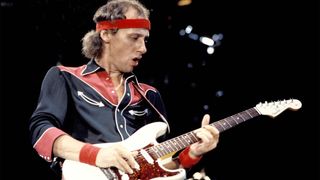 Mark Knopfler performing live onstage, playing Schecter-Suhr Strat guitar, wearing headband, circa 2000