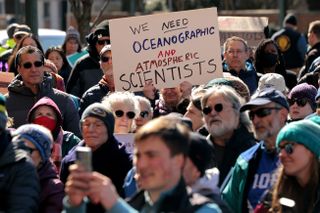 Many people at a protest; one person is holding up a sign that says "we need oceanographic and atmospheric scientists."