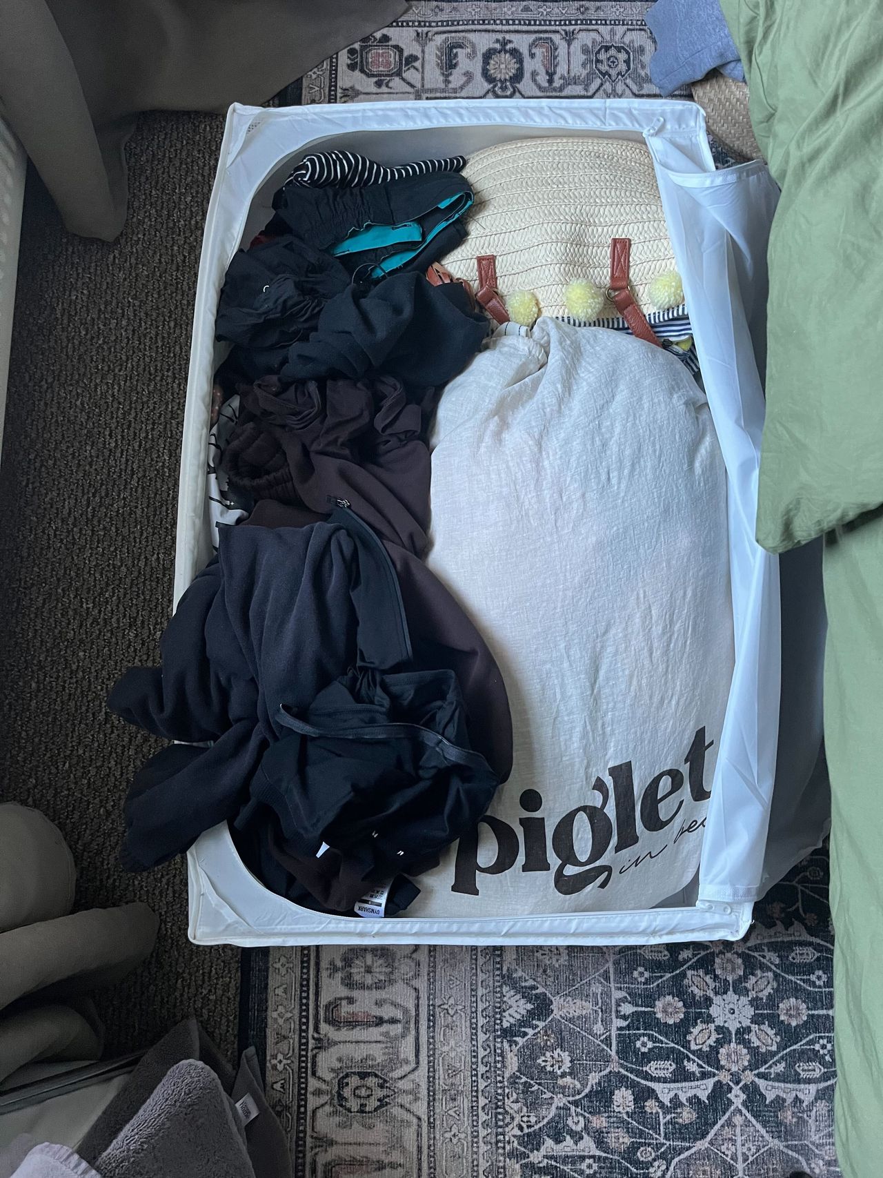 An under bed storage bag with lots of messy clothes piled inside