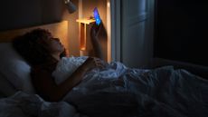 Woman looking at mobile phone in bed late at night, wondering does blue light affect sleep
