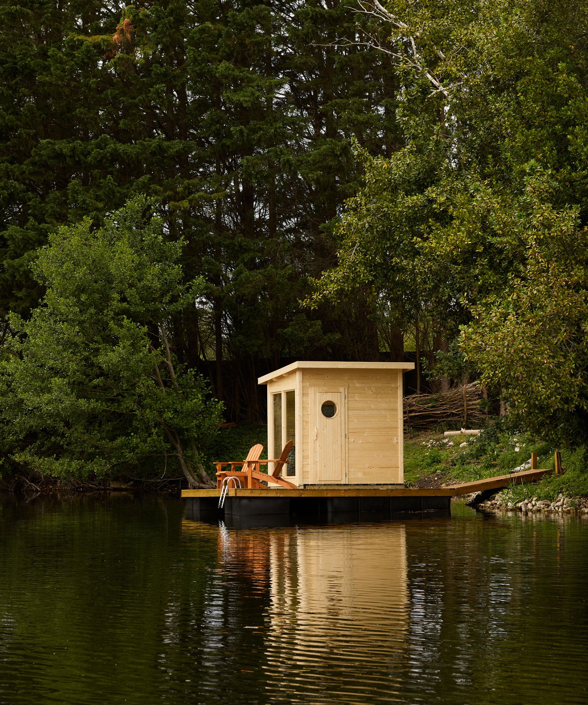 a lake in Normandy with a small wooden sauna built on a jetty with wooden loungers