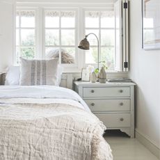 Neutral white painted bedroom with white and cream bedding and a chest of drawers next to it